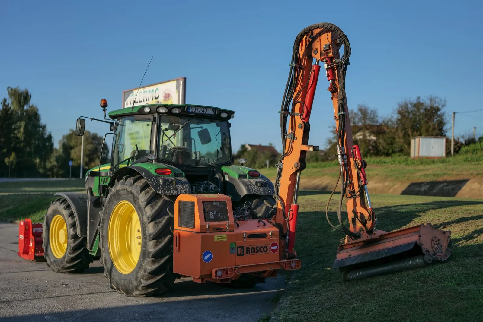 Tractor with mower attachment maintaining grass in rural Garešnica, Croatia under clear skies.